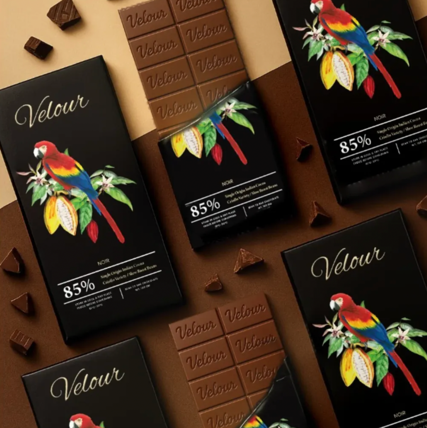 Velour chocolate bars with parrot illustrations on black packaging against a brown background